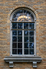 Retro window in brick house with marble ledge and cracked paint, with lit chandelier showing through top arched stained glass portion