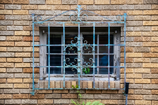 Ornate metal grill with gungy paint over an old window in a brick building - close-up