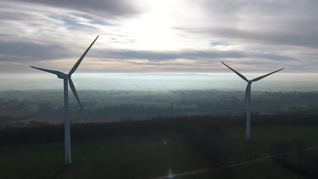 Aerial back tracking wind turbines electric green power generator. Misty morning landscape