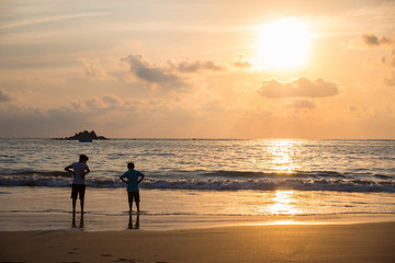 Two young boys wading in the ocean, on the beach towards sunset.