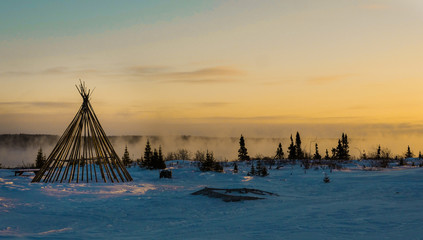 Obraz premium Cree tipi oprawione o zmierzchu nad mglistą rzeką w odległym północnym lesie borealnym Quebecu