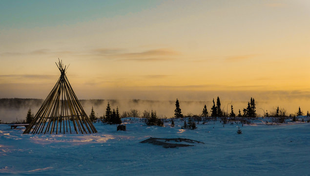 Cree teepee frame at dusk by a misty river in the remote northern boreal forest of Quebec