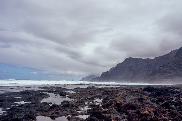 Tenerife: Black stone beach with a view of the cloud-covered mountains on a rainy day