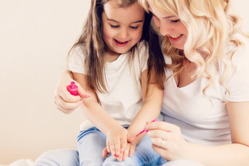 Happy mom and little girl sitting at home together and paiting their nails themselves
