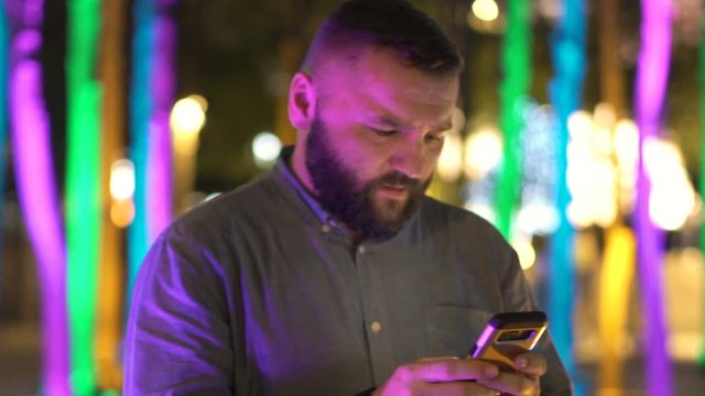 Young man texting on smartphone standing in the city at night
