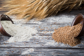 Two clay plates on a wooden table. Wheat and flour spill out of the plates.