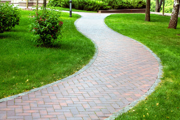 Pedestrian pavement paved with tiles, wavy pavement for walking in a park area with a green lawn.