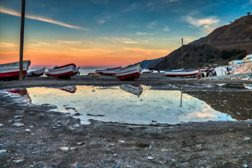 Fototapeta na wymiar Dramatic sunset with boats reflecting in the water on the beach of Oued Laou, Chaouen province, Morocco