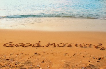 The word of good morning writing on sand beach with waves blue ocean.