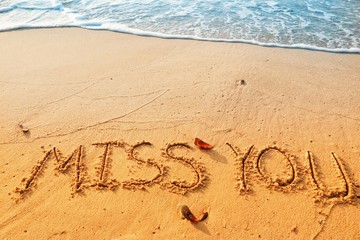 Valentine's day concept, miss you writing on sand beach with waves blue ocean.