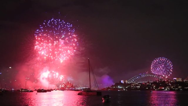 Red, blue colourful light balls during New Year fireworks in Sydney over still waters of Sydney harbour at night over major city CBD landmarks.
