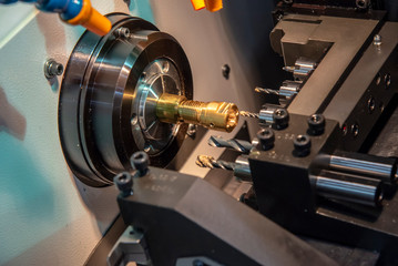 The CNC lathe or turning machine cutting the thread  at the brass  shaft.Hi-technology manufacturing process.