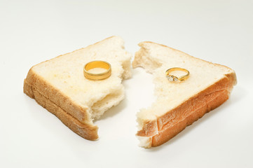 Two separate wedding rings with torn bread meaning to the word divorce.