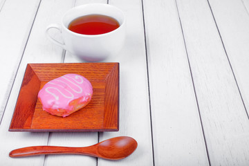 A cup of tea and sweet donut on wooden plate over  wooden tabletop with wooden  spoon. Celebration concept