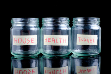Glass jars with text on black background: house,health, travel,