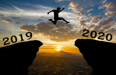 A young man jump between 2019 and 2020 years over the sun and through on the gap of hill ...