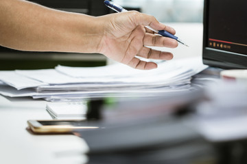 Businessman hands holding pen working in Stacks of paper files searching information business report papers and piles of unfinished documents achieves on laptop computer desk in modern office