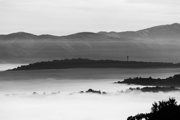 Fog filling a valley in Umbria (Italy), with layers of mountains and hills, trees in the foreground and Montefalco town at the distance