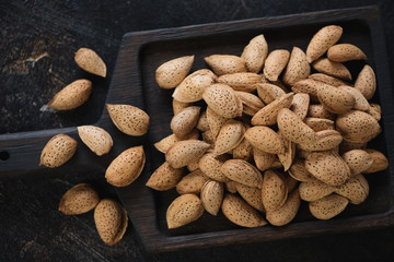 Close-up of almond nuts on a black wooden serving tray, view from above, studio shot