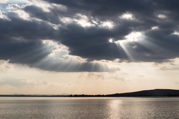 Obraz premium Beautiful sunset on a lake, with sunrays coming down under an overcast sky