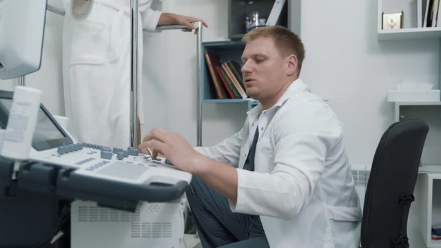 Phlebologist uses ultrasound machines to scan patient's veins on legs, steadicam shot.