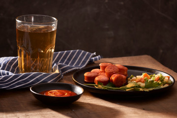 Glass of delicious beer with grilled sausages on wooden table