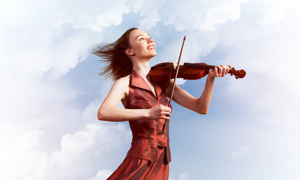 Woman violinist in red dress playing melody against cloudy sky