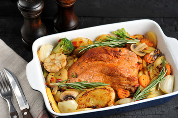 Pork ham baked with vegetables. In the frame of cloth napkin, cutlery, a set for spices. Dark background. Close-up. Macro shooting. 