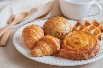 Various baked bread on plate and coffee cup.