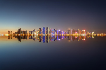 Weites Panorama der beleuchteten Skyline von Doha in Katar mit Spiegelung im Wasser