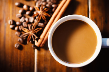 Cup of coffee with cinnamon stick, star anise and roasted coffee beans on wooden table, hot drink