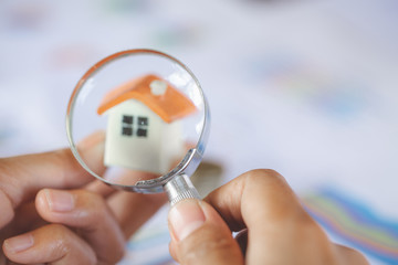 Close-up Of A Businessperson's Hand Looking At House Model Through Magnifying Glass, House searching concept with a magnifying glass