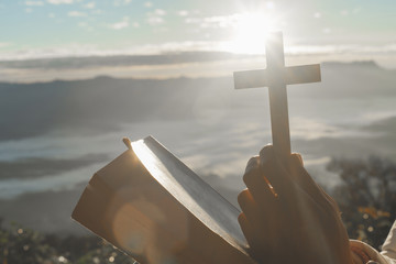 Christian woman praying on the mountain with morning sunrise. Hands crossed and Holy Bible . Background