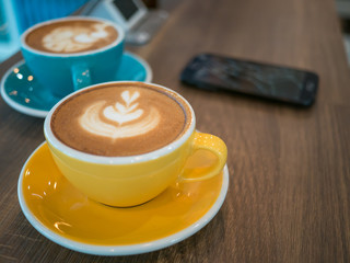 Hot coffee late art in cup on blur coffee cup and mobile phone background,