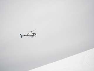 White helicopter flies over snowy mountains on a cloudy day
