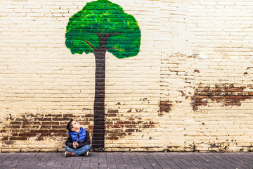 Little kid seated under a tree painted on a wall