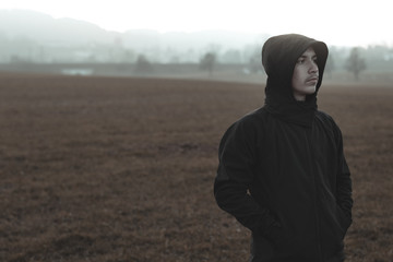 thinking male with hoodie standing outside at field