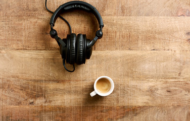 Black headphones and a cup of coffee on rustic wooden background. Top view, Copy space. 