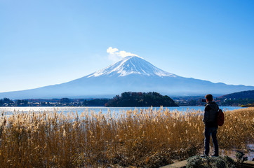 Photographer man standing outdoor photography by mobile amidst beautiful nature of Mt. Fuji at Yamanashi in Japan with lake kawaguchiko. Travel and Attractions Concept.