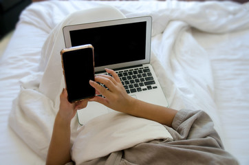 Concentrated young Asian girl looking at her smartphone lying on the bed in bedroom. Technology and internet concept. Copy space. Preteen or school age girl using mobile phone in the morning