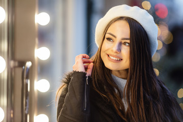 Fototapeta premium Pretty girl stand on the street wear black hat, look at window store and make funny expressions on her face. - Image