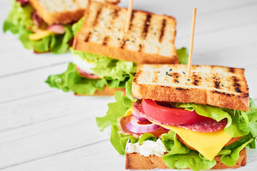 Three sandwiches with ham, lettuce and fresh vegetables on a white background
