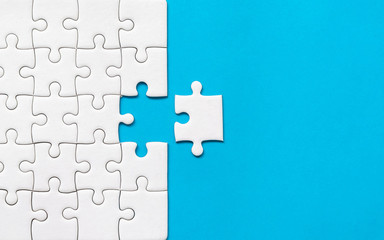 White jigsaw puzzle on blue background. Team business success partnership or teamwork.