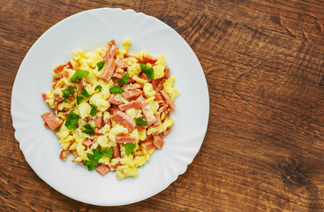 scrambled eggs with ham and cheese in white plate on wooden table background