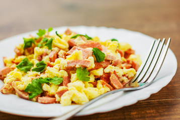scrambled eggs with ham and cheese in white plate on wooden table background