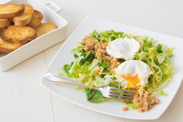 Classic French salad, great salad Lyonnaise. Dish with green leaves of lettuce, Dijon mustard sauce with pieces of fried bacon, grilled French bread, toasts and 2 poached eggs on the top.