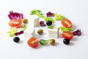 Greek salad, white Greek cheese, green and black olives, lettuce leaves, halfs of cherry tomato. White background. variations of salad leaves and feta myzithra cheese.