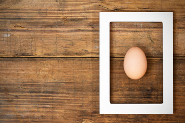 Frame with egg inside on brown wooden background texture