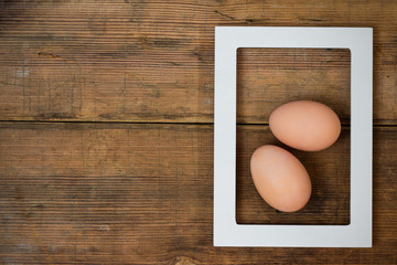 Frame with two eggs inside on brown wooden background texture