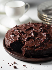 Ruined chococolate cake on a wooden plate. White porcelain cups and plates in bokeh
